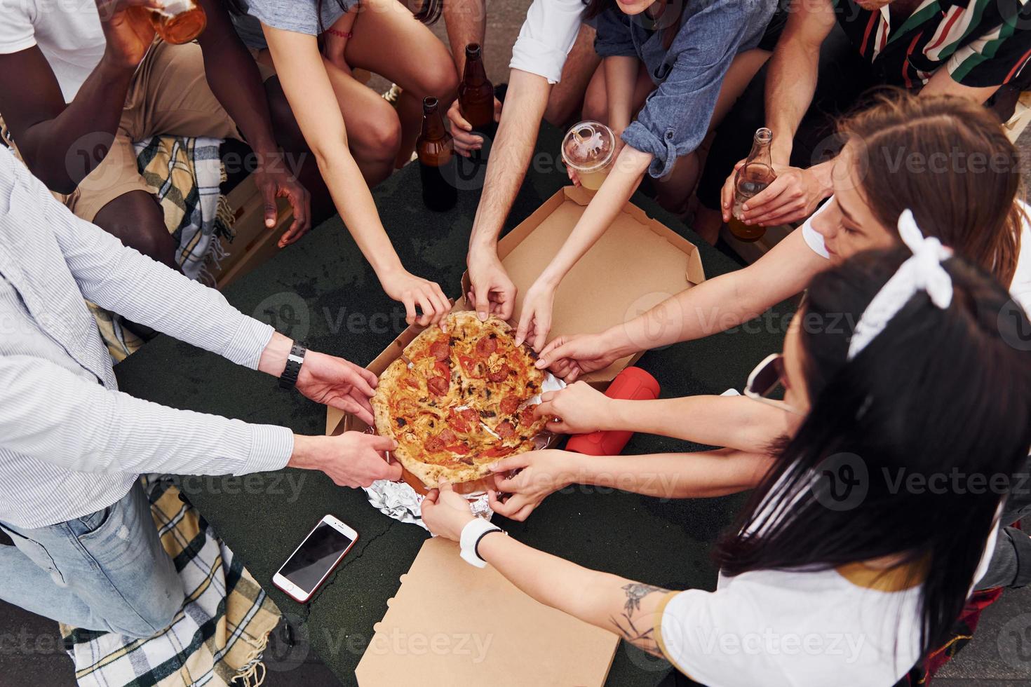 con delizioso Pizza. gruppo di giovane persone nel casuale Abiti avere un' festa a tetto insieme a giorno foto