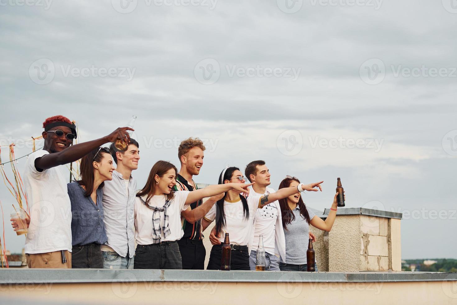 decorato posto. nuvoloso tempo atmosferico. gruppo di giovane persone nel casuale Abiti avere un' festa a tetto insieme a giorno foto