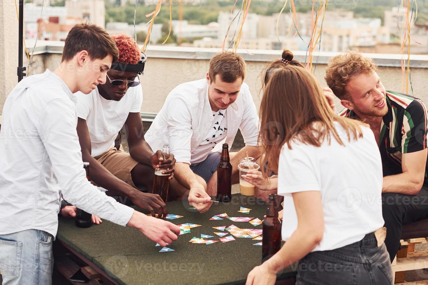 giocando gioco e seduta di il tavolo. gruppo di giovane persone nel casuale Abiti avere un' festa a tetto insieme a giorno foto