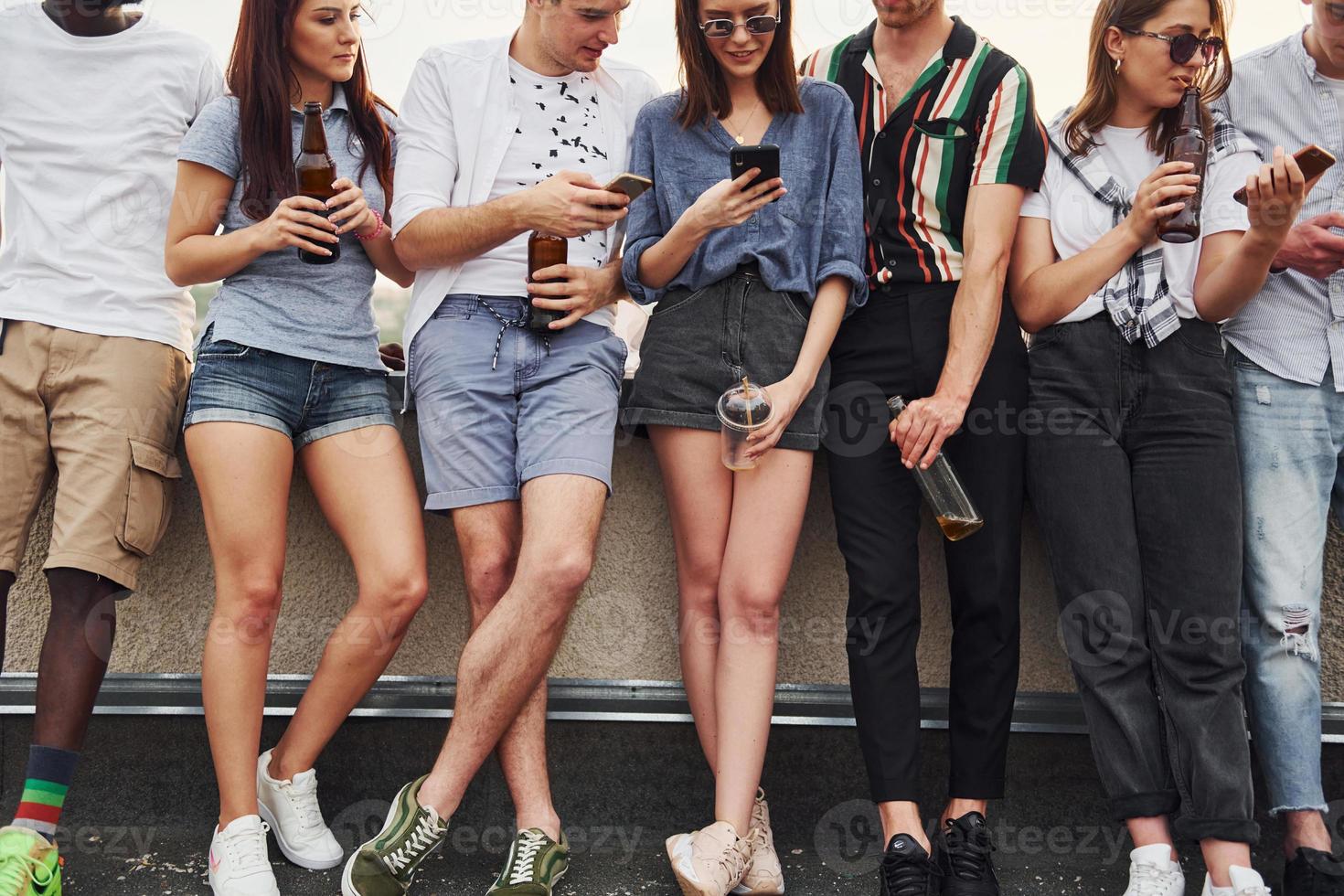 in piedi con alcool a il bordo di tetto. gruppo di giovane persone nel casuale Abiti avere un' festa insieme a giorno foto