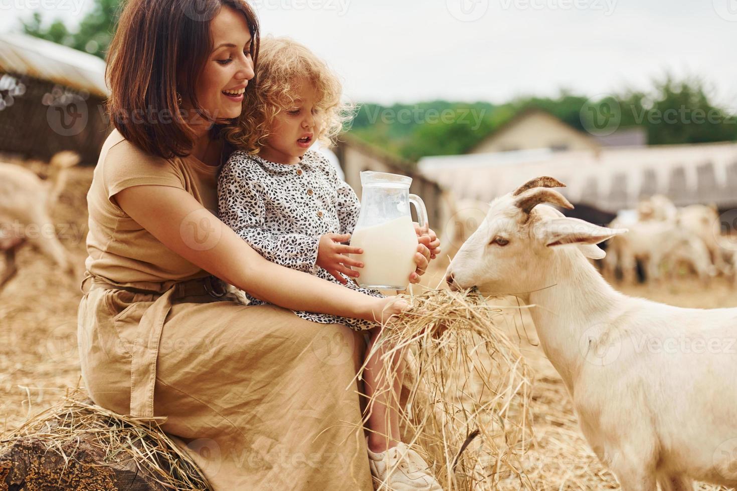 fresco naturale latte. giovane madre con sua figlia è su il azienda agricola a estate con capre foto