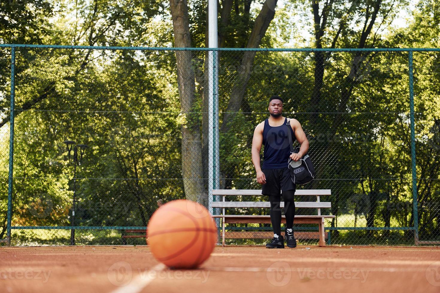 bellissimo verde alberi su sfondo. africano americano uomo giochi pallacanestro su il Tribunale all'aperto foto