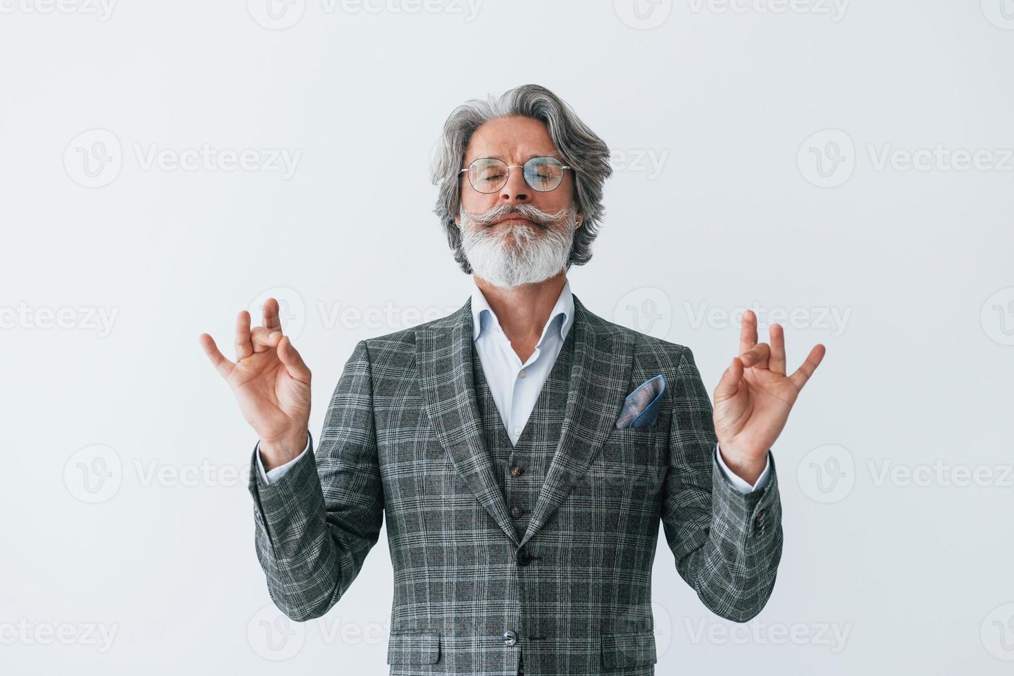 nel elegante Abiti. in piedi contro bianca parete. anziano elegante moderno uomo con grigio capelli e barba in casa foto