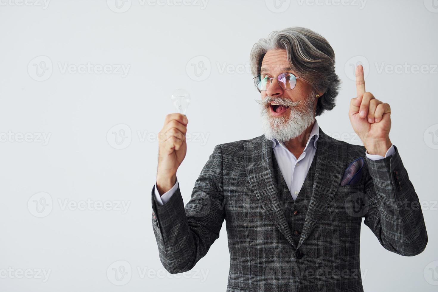con leggero lampadina nel mani. anziano elegante moderno uomo con grigio capelli e barba in casa foto