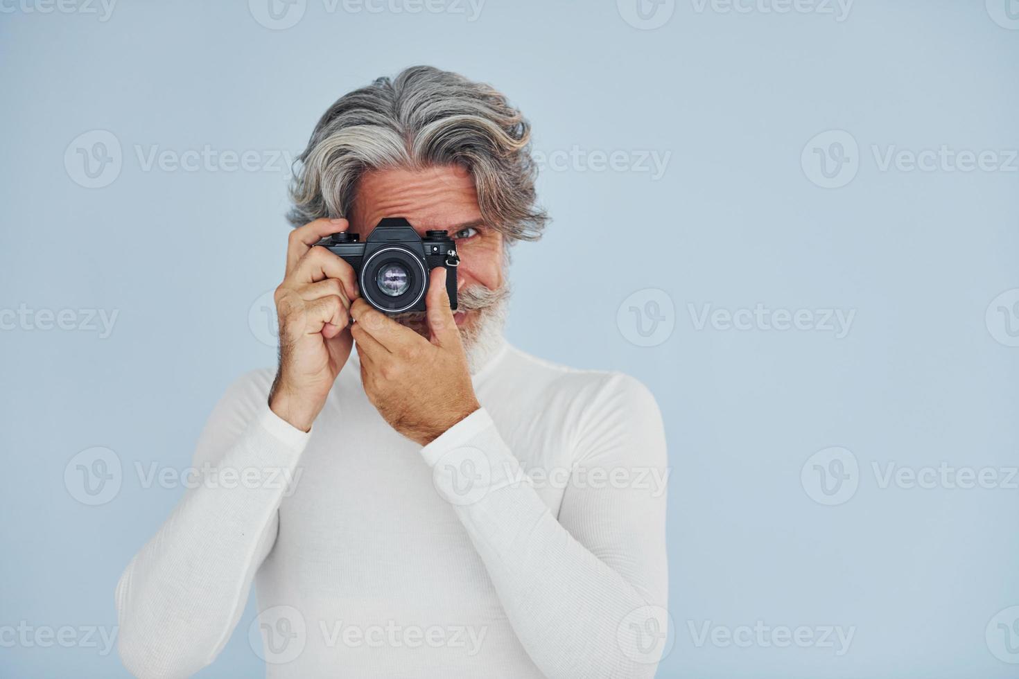 fotografo con Vintage ▾ telecamera. anziano elegante moderno uomo con grigio capelli e barba in casa foto