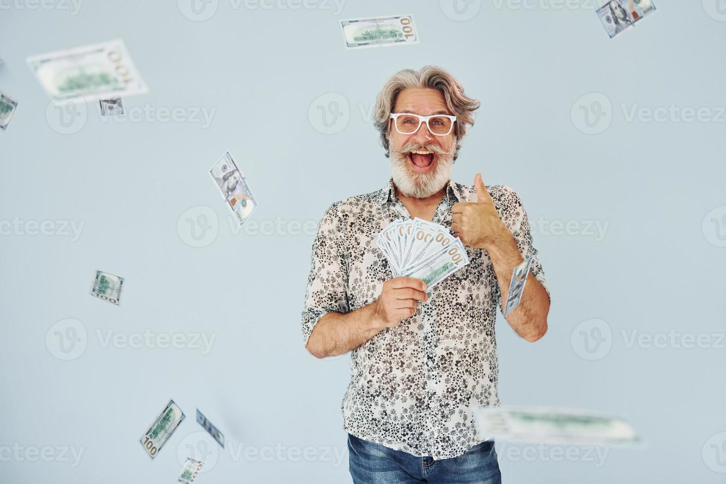 milionario con denaro contante nel mani. anziano elegante moderno uomo con grigio capelli e barba in casa foto