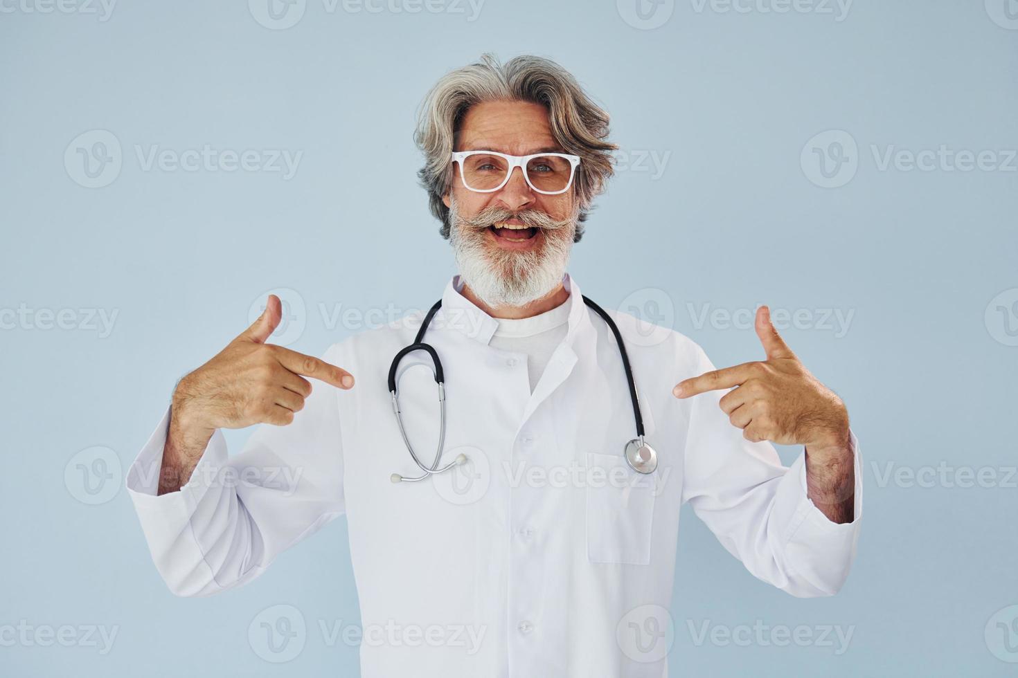 professionale positivo medico. anziano elegante moderno uomo con grigio capelli e barba in casa foto