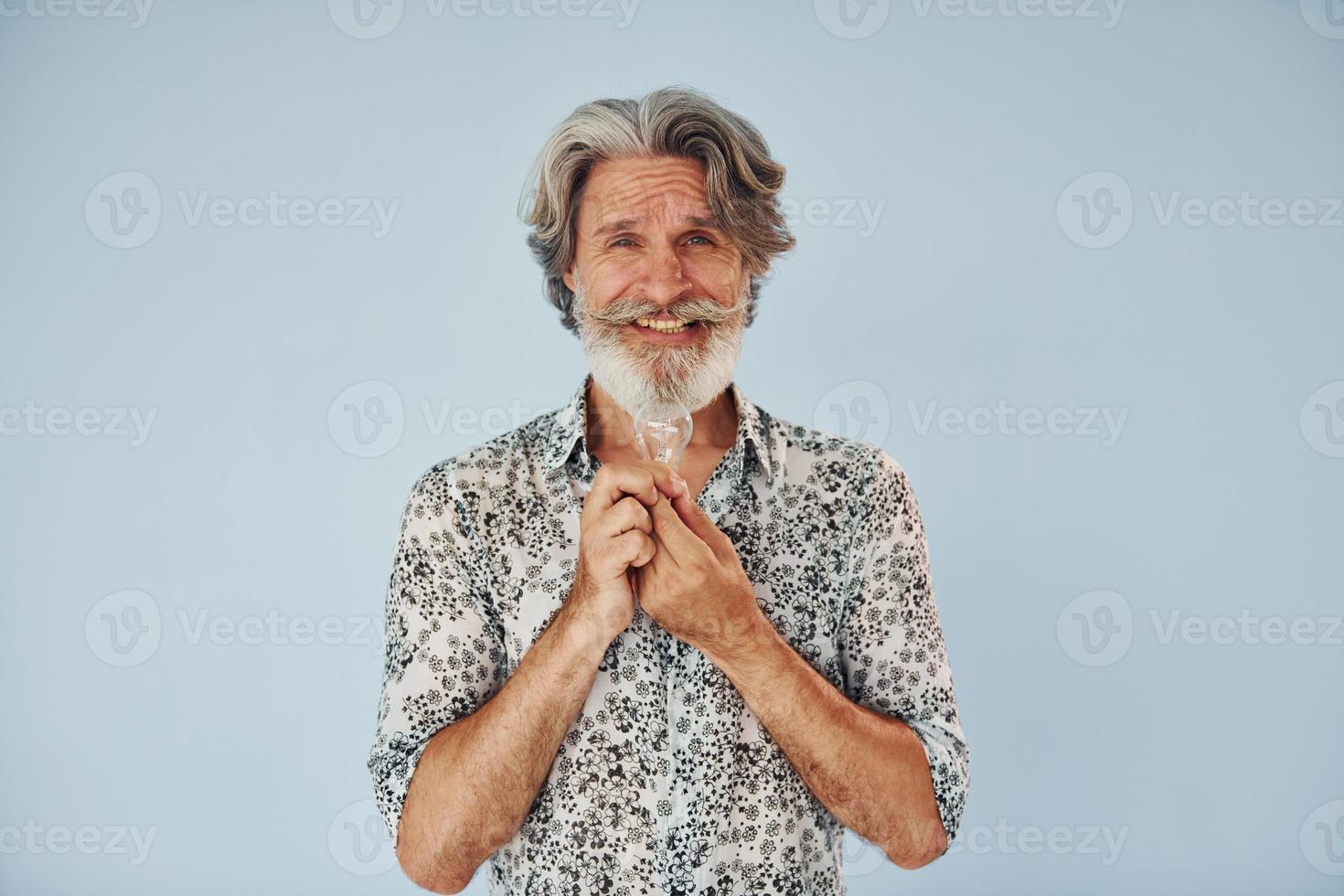 detiene leggero lampadina nel mani. concezione di idee e ispirazione. anziano elegante moderno uomo con grigio capelli e barba in casa foto