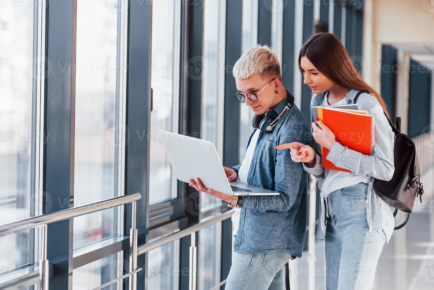 Due giovane alunno amici insieme nel un' corridoio di un' Università con il computer portatile nel mani foto