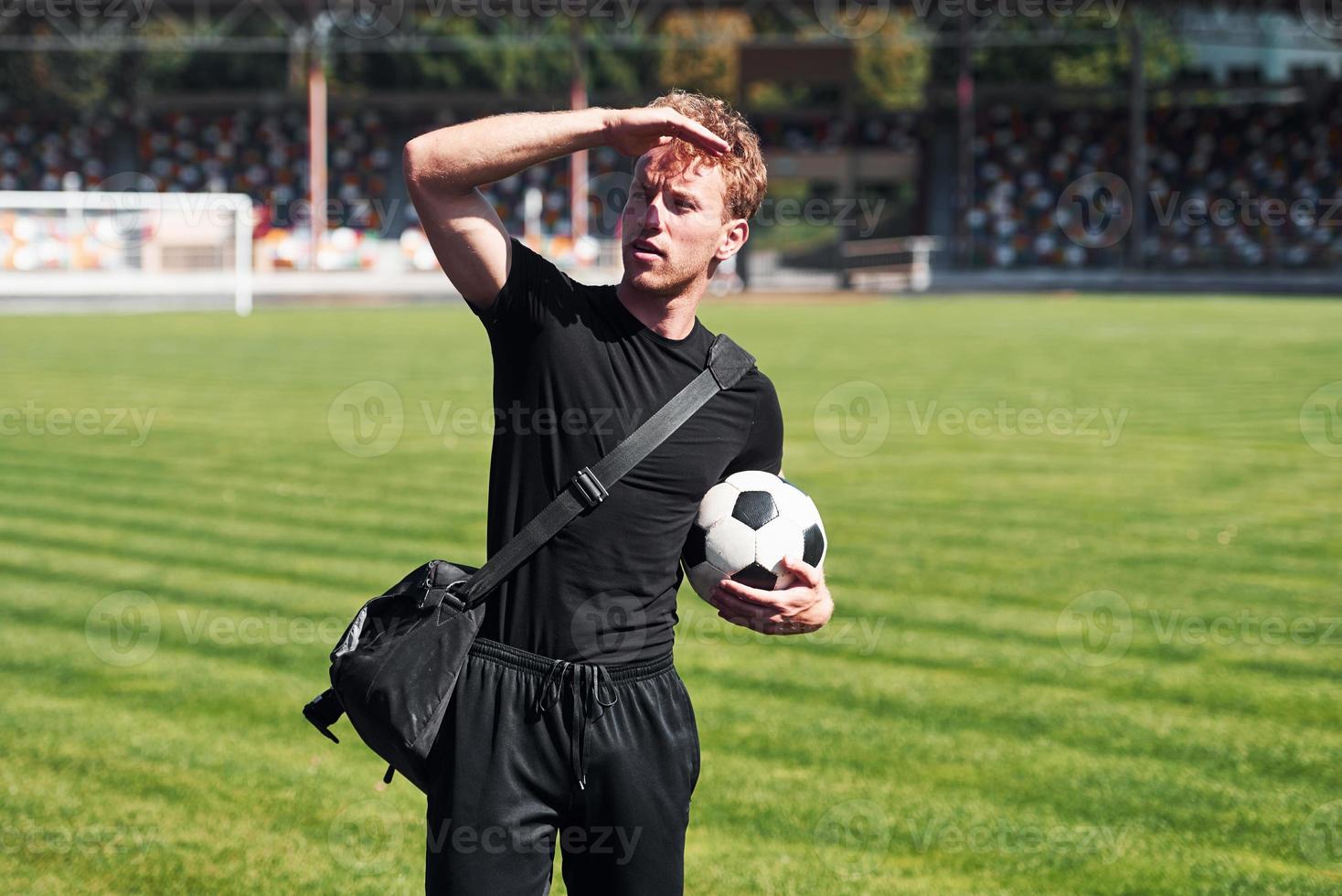 calcio giocatore su il campo. allegro giovane tipo nel nero camicia e pantaloni all'aperto a giorno foto