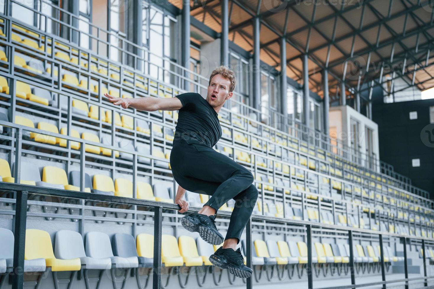 salto e fare parkour su il gradinate. allegro giovane tipo nel nero camicia e pantaloni all'aperto a giorno foto