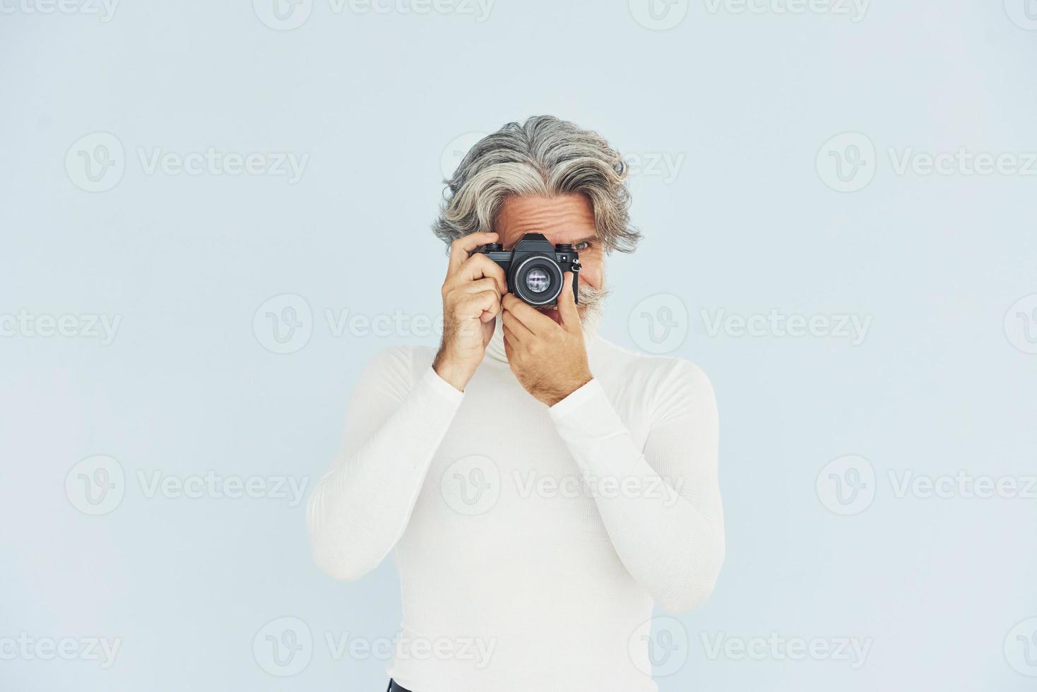 fotografo con Vintage ▾ telecamera. anziano elegante moderno uomo con grigio capelli e barba in casa foto