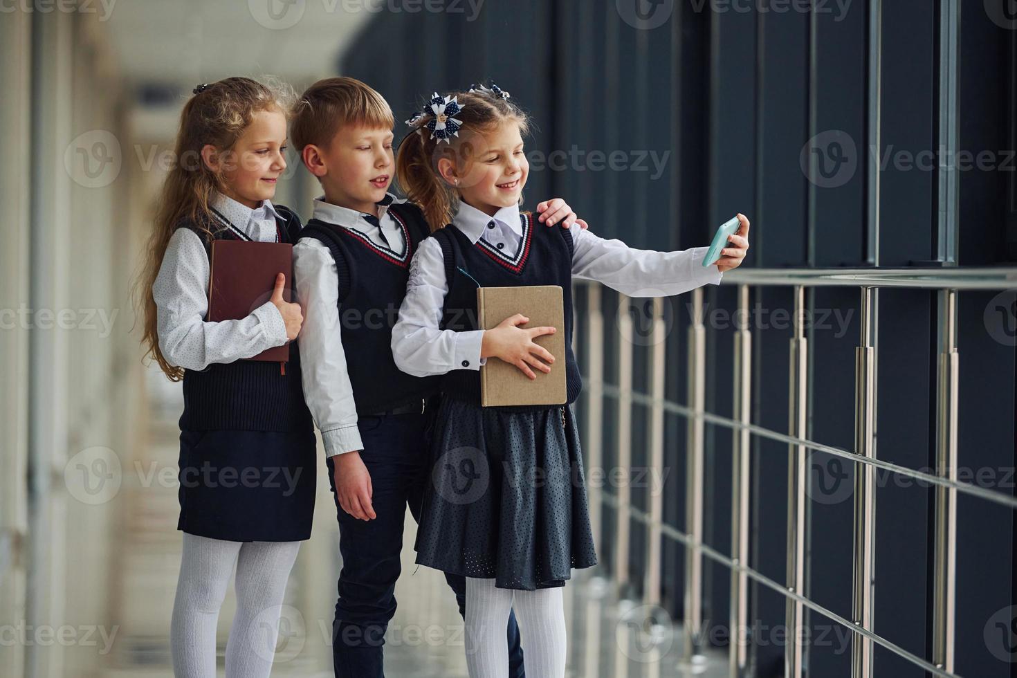 scuola bambini nel uniforme insieme con Telefono e fabbricazione autoscatto nel corridoio. concezione di formazione scolastica foto