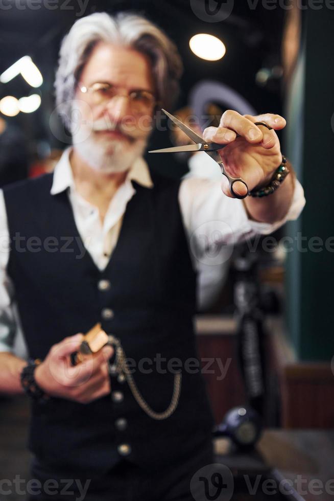 detiene barbiere attrezzatura. elegante moderno anziano uomo con grigio capelli e barba è in casa foto