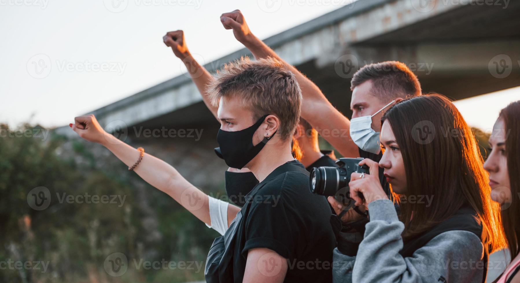 fotografo con telecamera. gruppo di protestare giovane persone quello in piedi insieme. attivista per umano diritti o contro governo foto