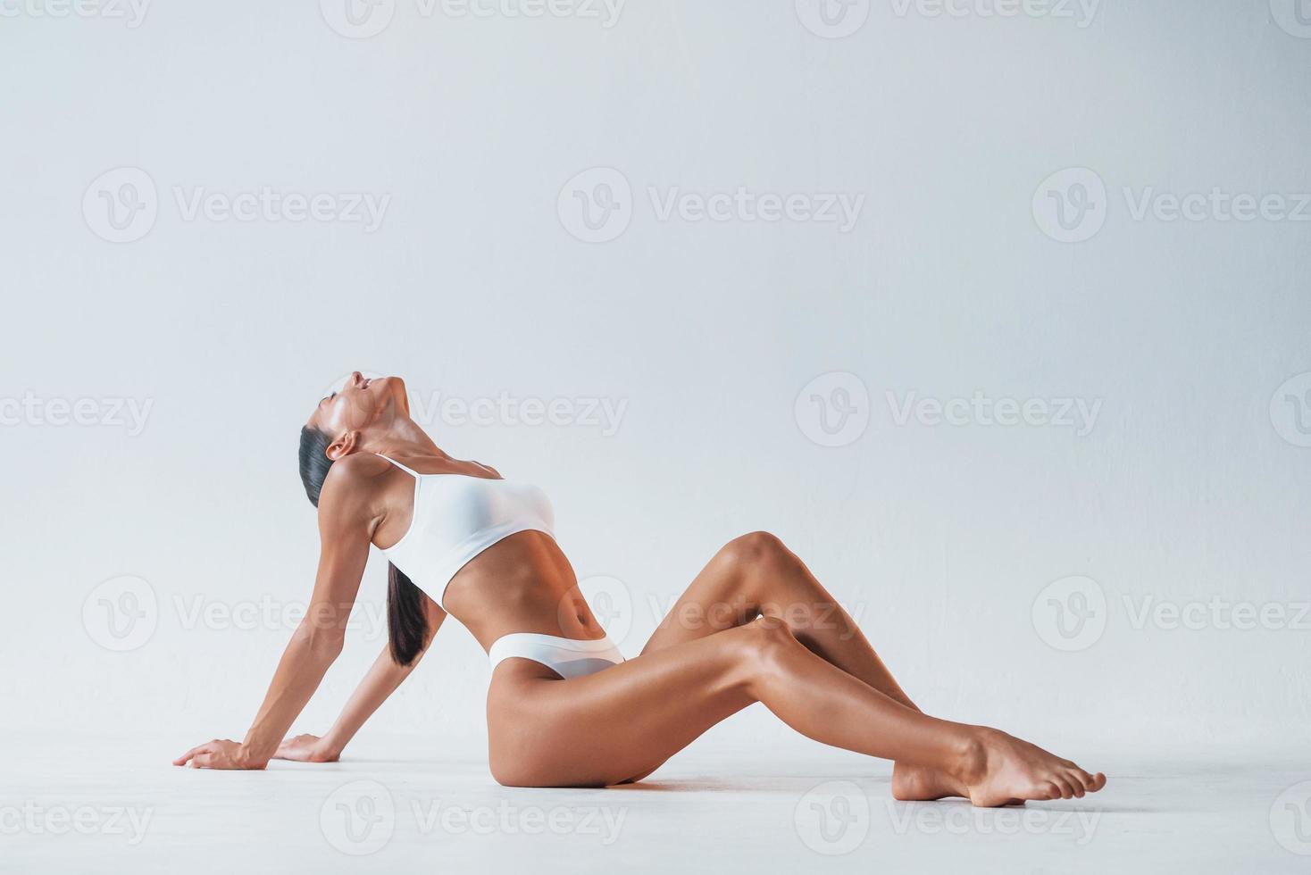 seduta su il pavimento. bellissimo donna con sottile corpo nel biancheria intima è nel il studio foto