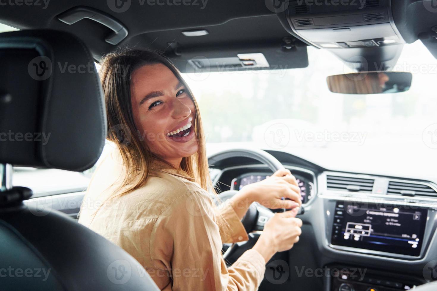 autista sembra indietro e sorridente. alla moda bellissimo giovane donna e sua moderno automobile foto