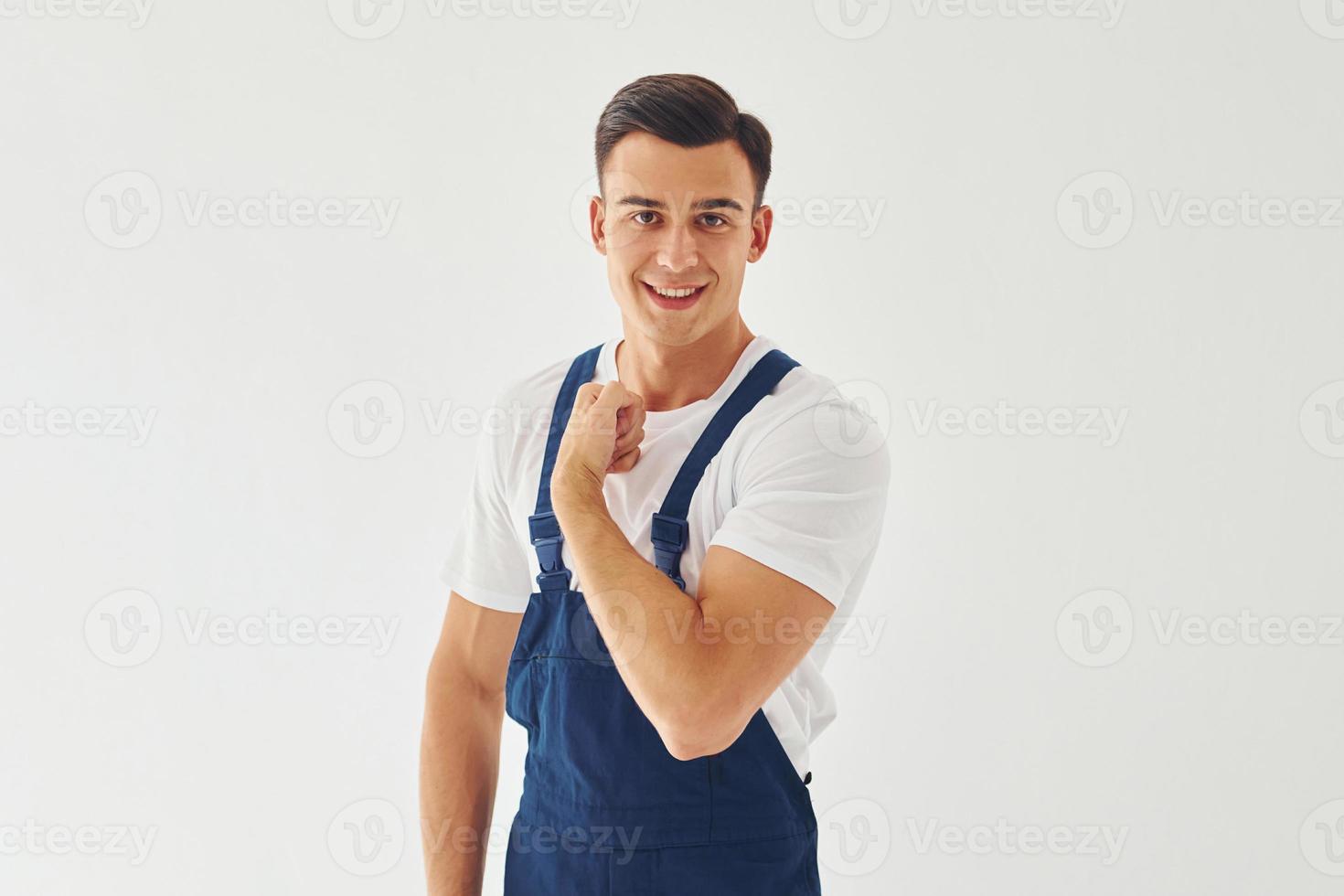 Spettacoli bicipite. pronto per opera. maschio lavoratore nel blu uniforme in piedi dentro di studio contro bianca sfondo foto