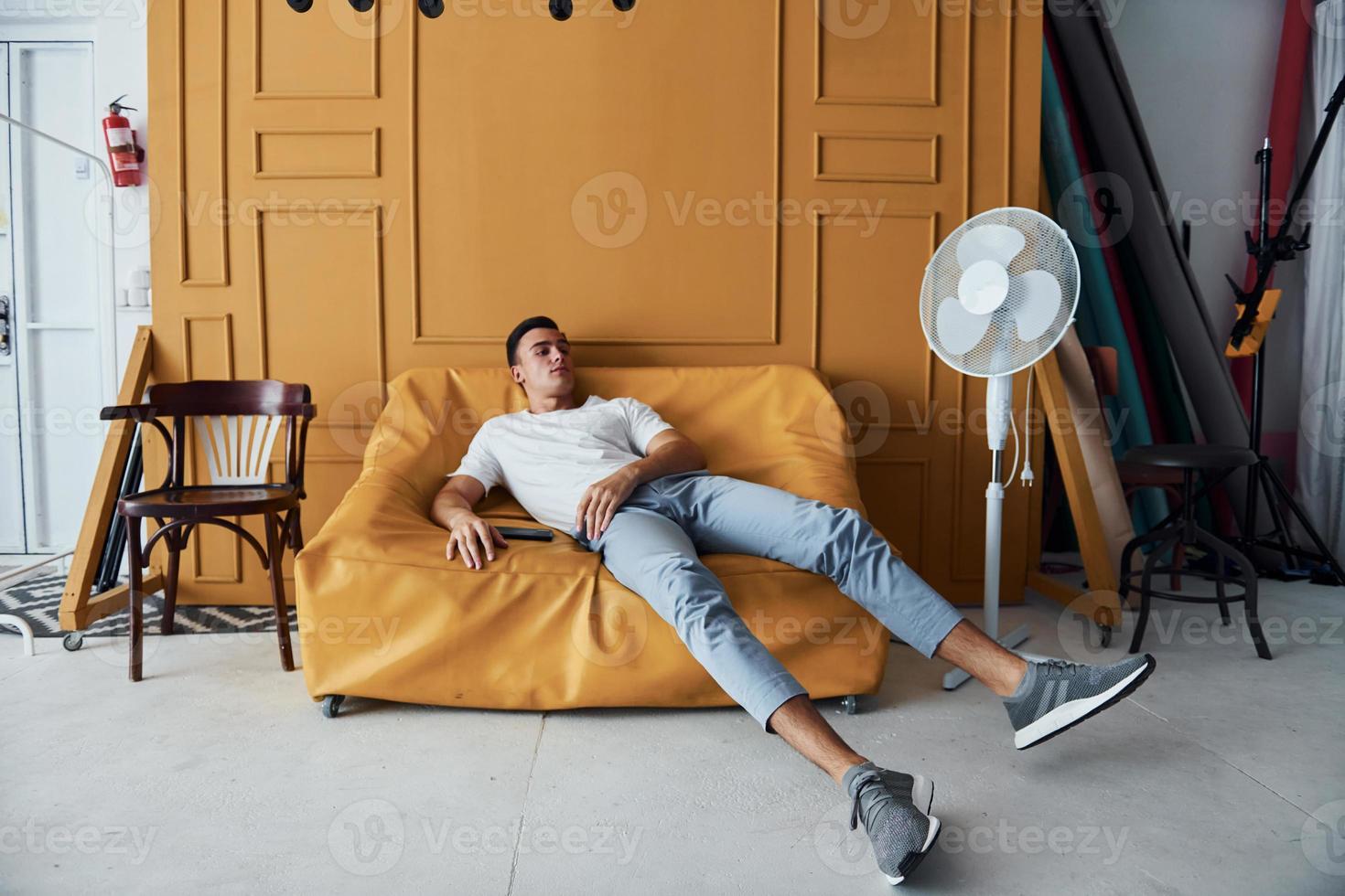 giovane tipo con elegante taglio di capelli e nel casuale Abiti seduta in casa nel camera con arancia colorato interno foto