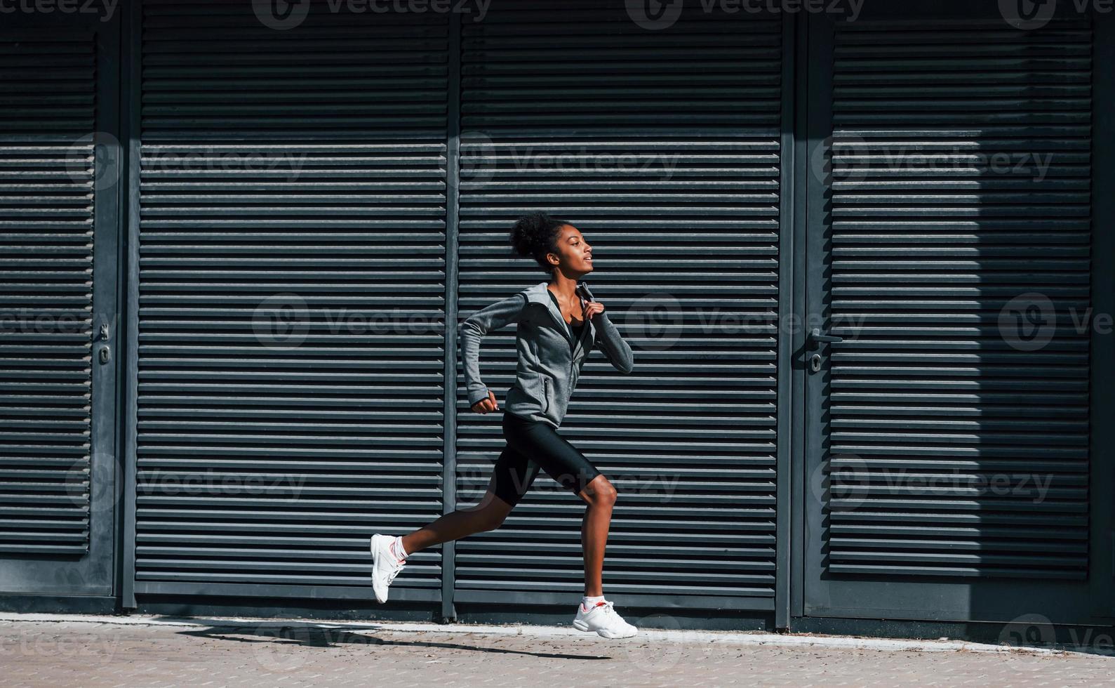 lato Visualizza di giovane africano americano donna nel allegro Abiti quello corre vicino parete foto