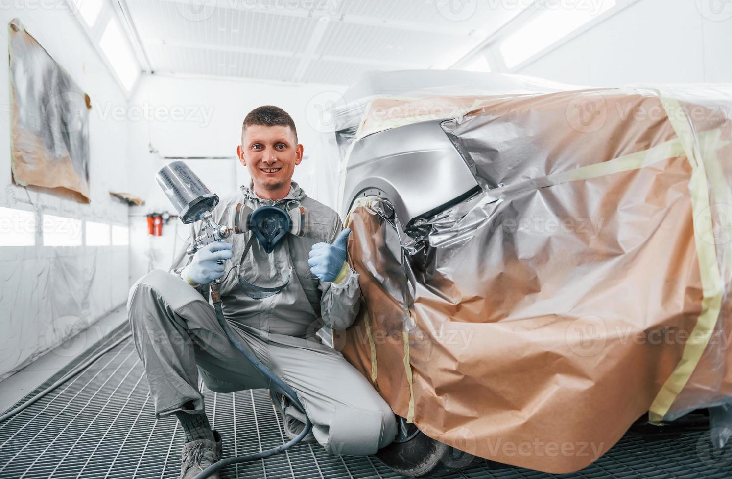 si siede vicino appena dipinto macchina. caucasico automobile riparatore nel uniforme lavori nel box auto foto