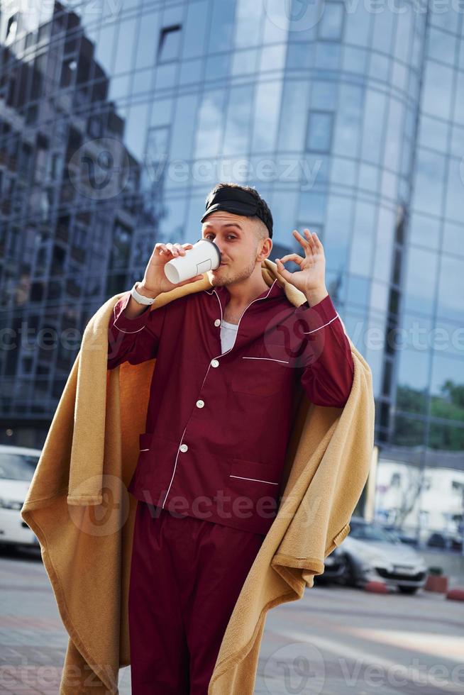 mattina caffè tazza. giovane uomo nel pigiama è all'aperto su il strada. si sente assonnato foto