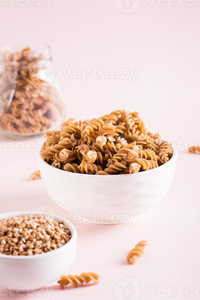 crudo pasta a partire dal grano saraceno Farina nel un' ciotola e semole nel un' ciotola su un' rosa sfondo. verticale Visualizza foto