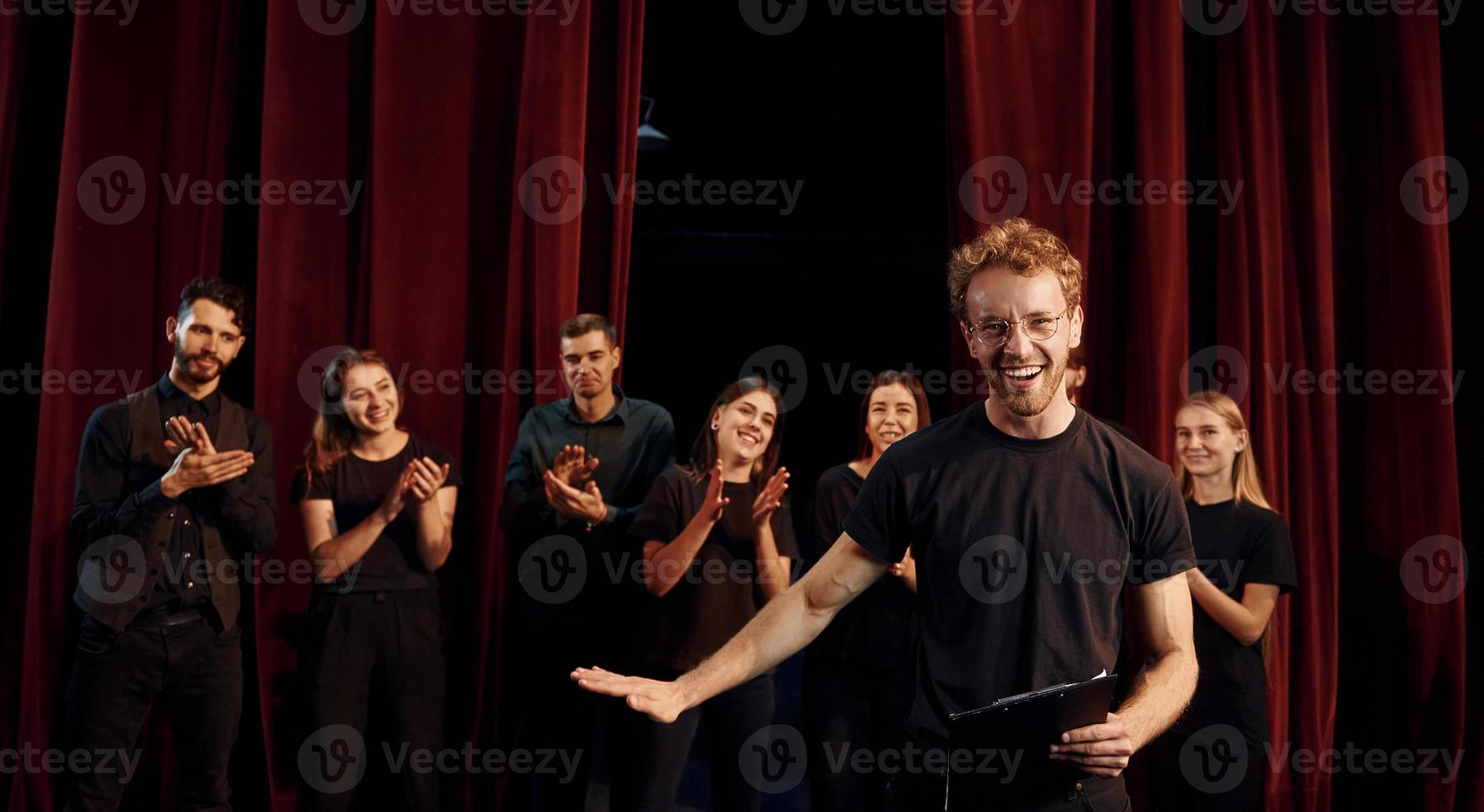 uomo con bloc notes pratica il suo ruolo. gruppo di attori nel buio colorato Abiti su prova nel il Teatro foto