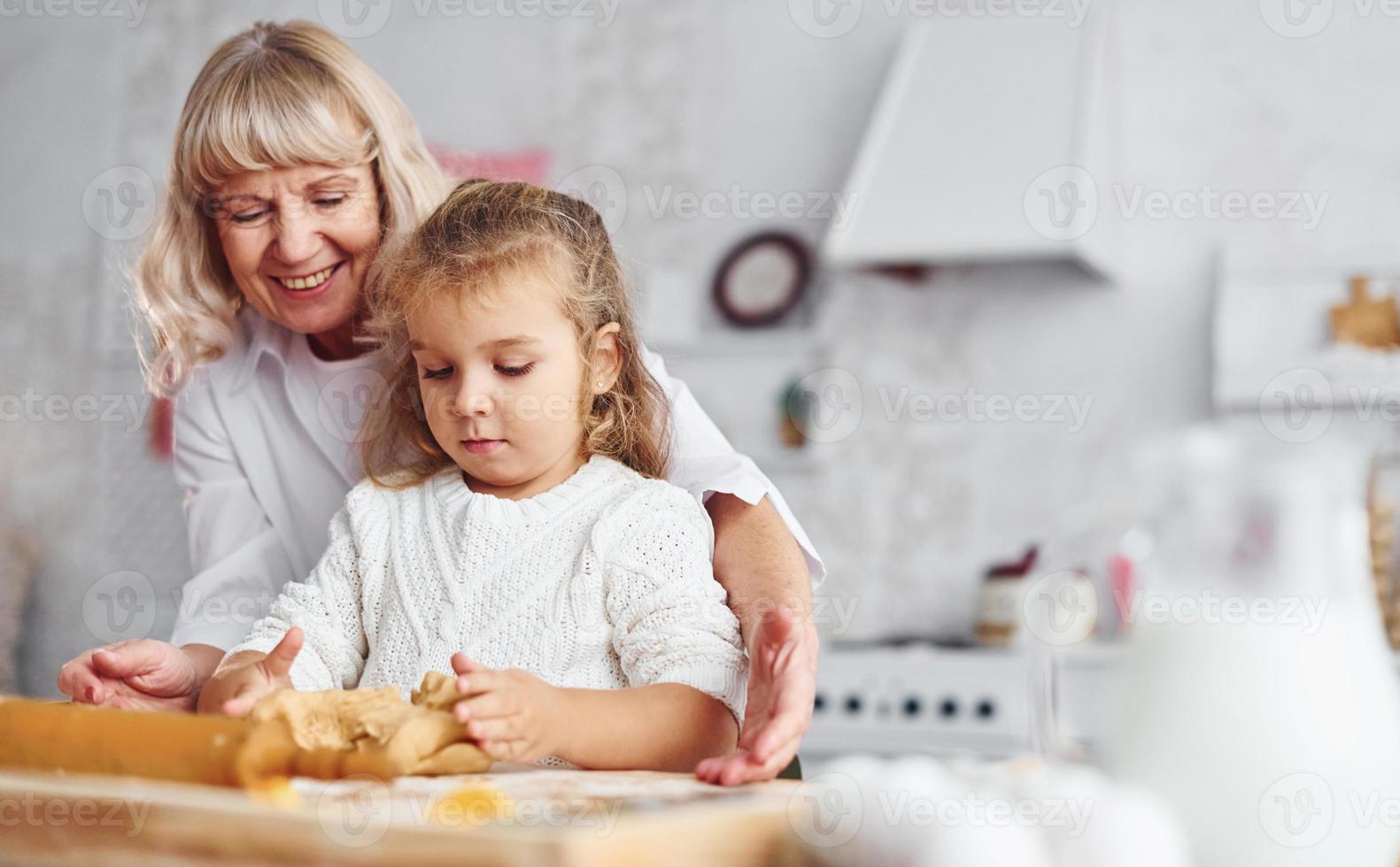 impasta il Impasto. anziano nonna con sua poco nipotina cuochi dolci per Natale su il cucina foto