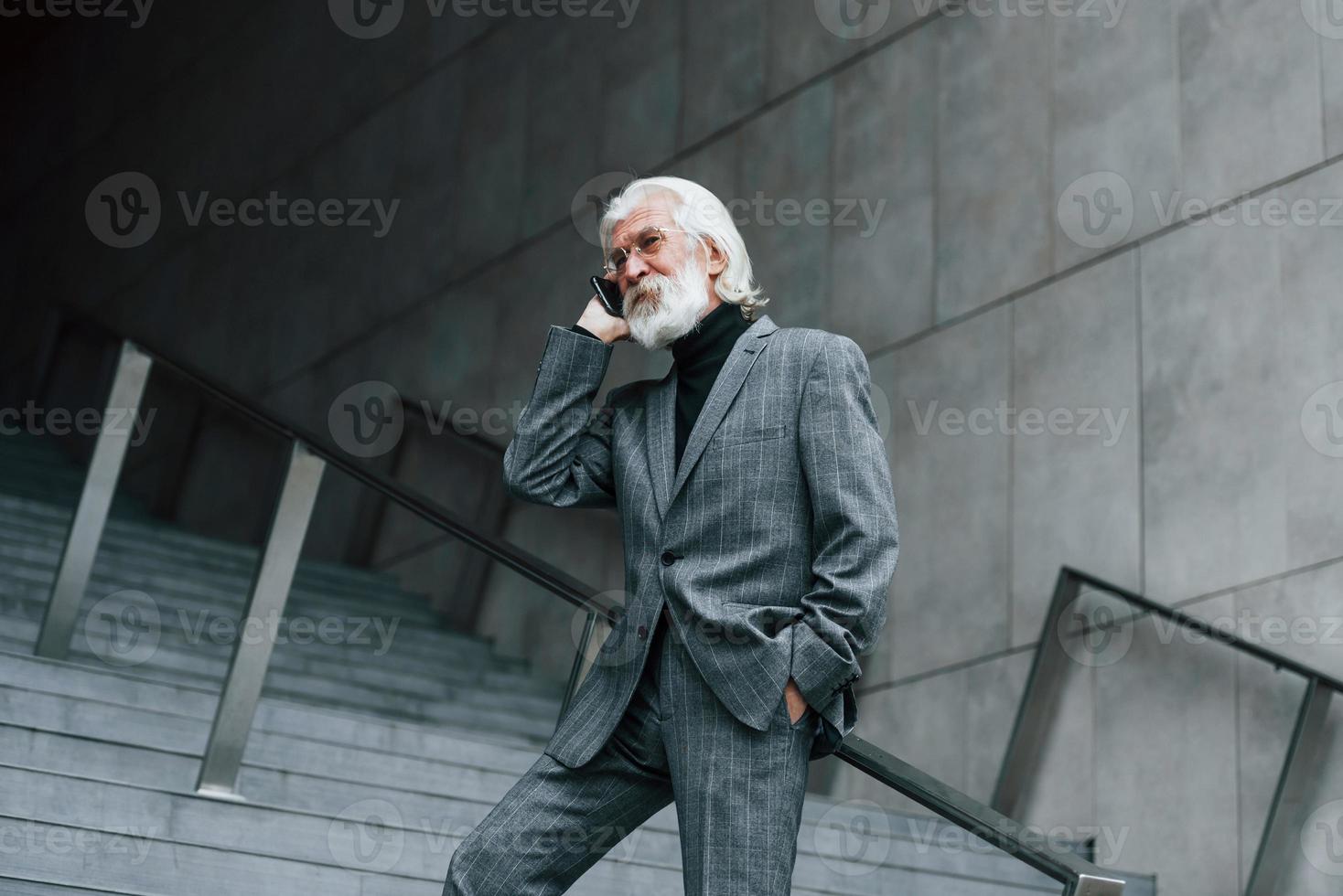 anziano uomo d'affari nel formale Abiti, con grigio capelli e barba è all'aperto parla di Telefono foto