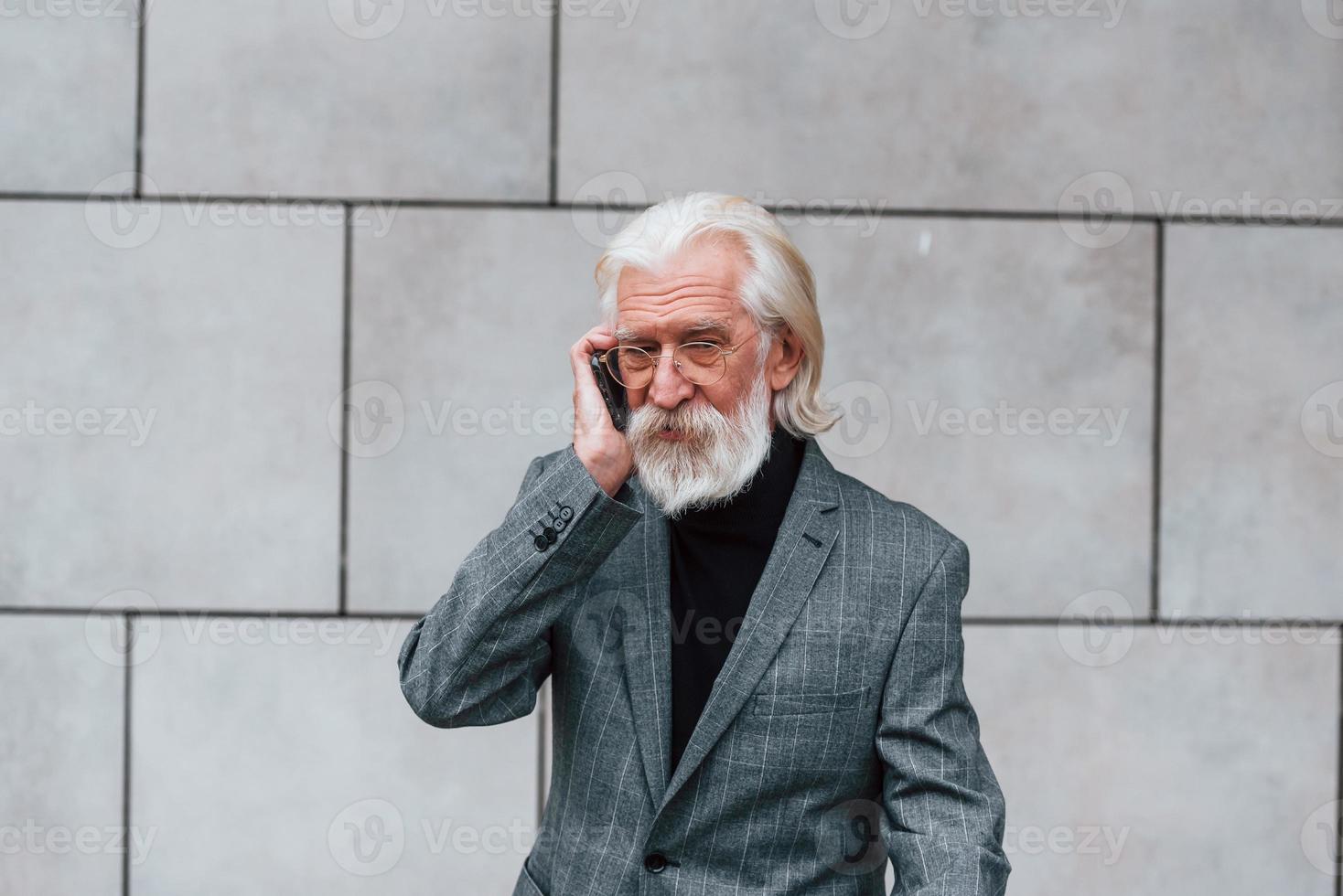 anziano uomo d'affari nel formale Abiti, con grigio capelli e barba è all'aperto parla di Telefono foto