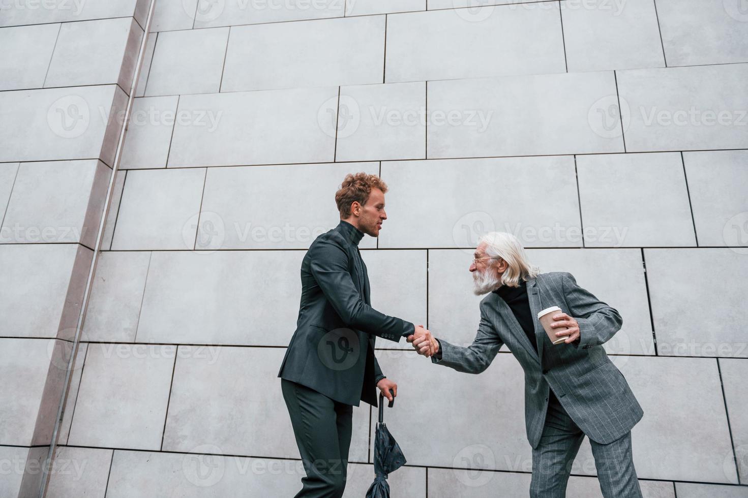 avendo un' incontrare. giovane tipo con anziano uomo nel elegante Abiti è all'aperto insieme. concezione di attività commerciale foto