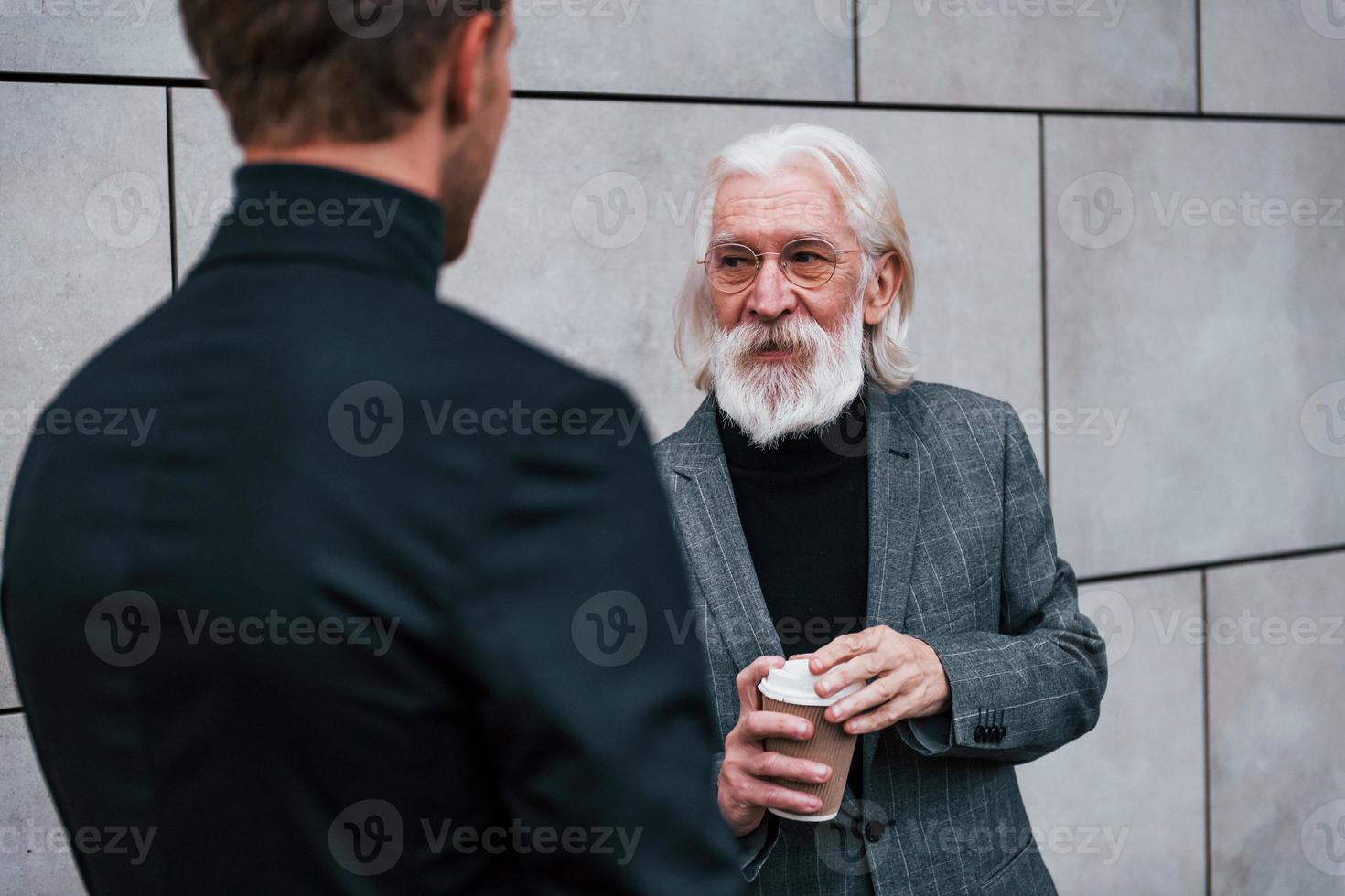 avendo un' incontrare. giovane tipo con anziano uomo nel elegante Abiti è all'aperto insieme. concezione di attività commerciale foto