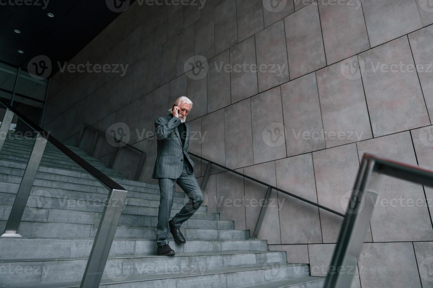 anziano uomo d'affari nel formale Abiti, con grigio capelli e barba è all'aperto parla di Telefono foto