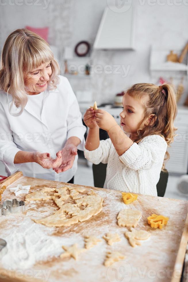 insegnamento processi. anziano nonna con sua poco nipotina cuochi dolci per Natale su il cucina foto