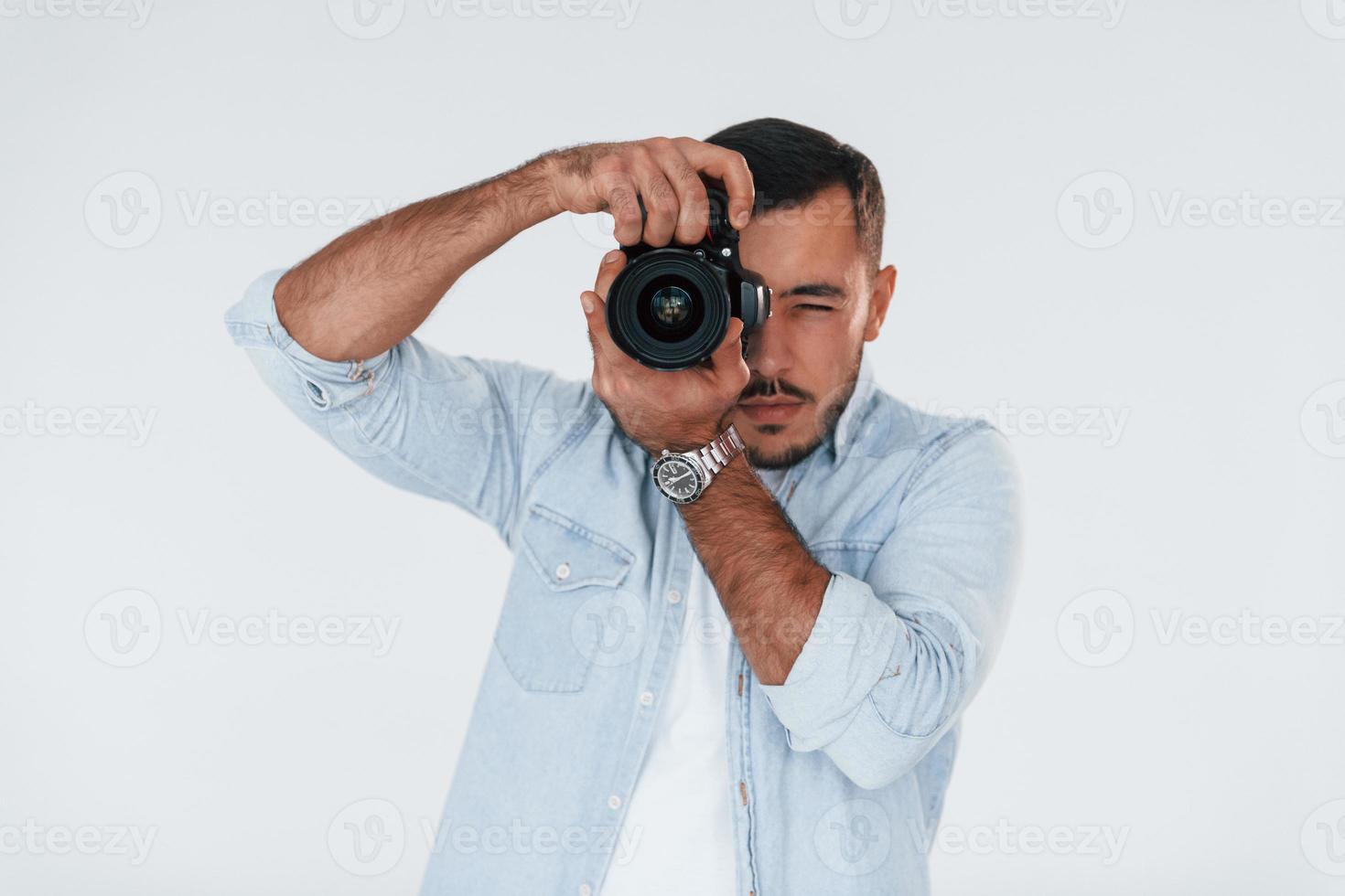 con professionale telecamera. giovane bello uomo in piedi in casa contro bianca sfondo foto