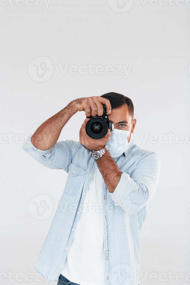 con professionale telecamera. giovane bello uomo in piedi in casa contro bianca sfondo foto