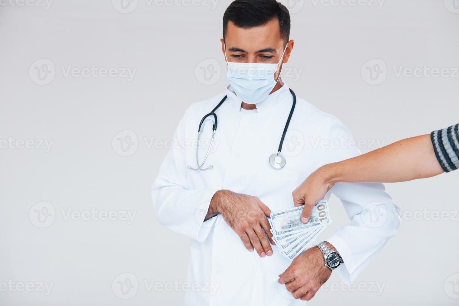 medico detiene i soldi. giovane bello uomo in piedi in casa contro bianca sfondo foto
