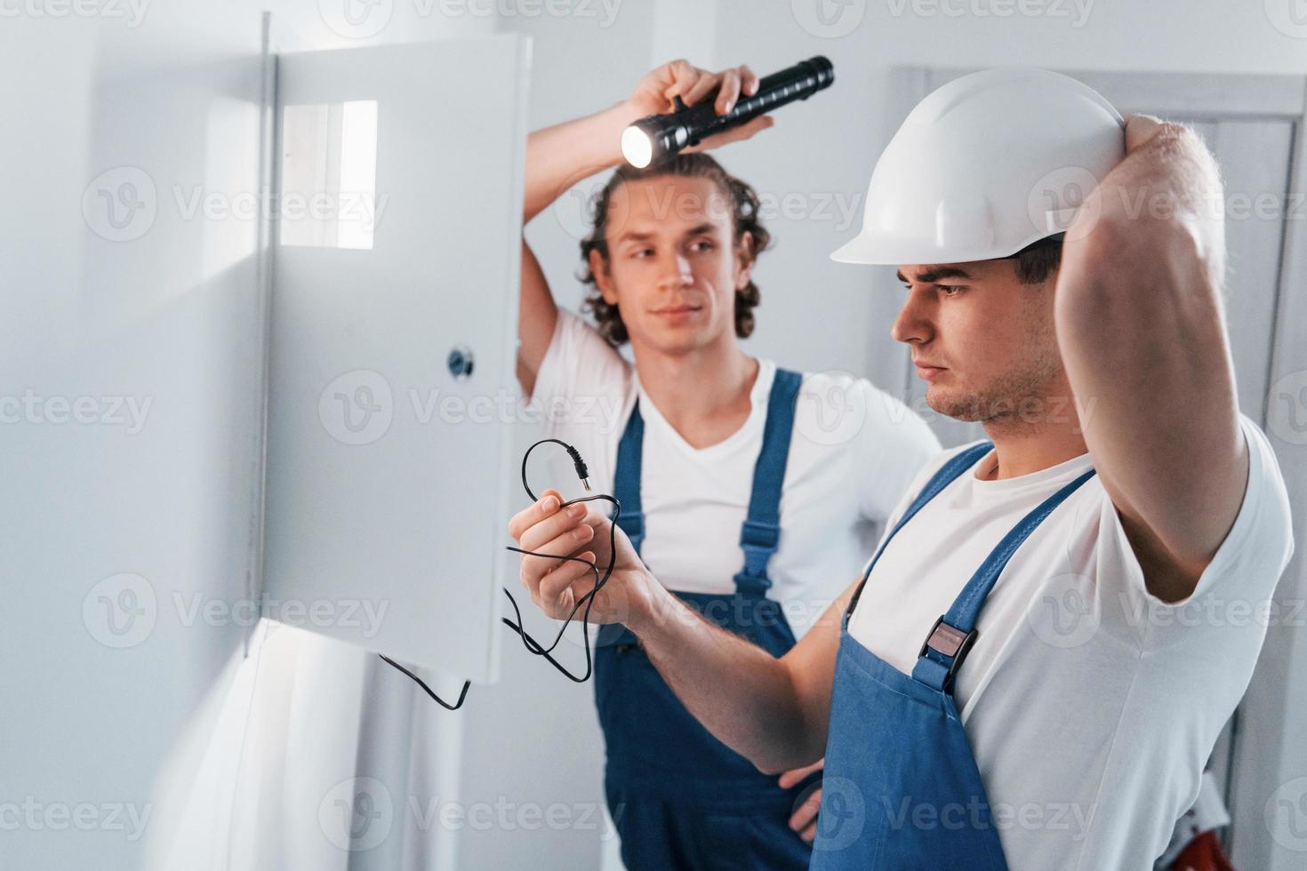 Due giovane maschio elettricisti lavori in casa insieme. utilizzando torcia elettrica foto