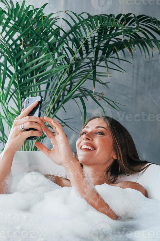 usi Telefono. bellissimo giovane donna avere gratuito tempo a casa nel il bagno foto