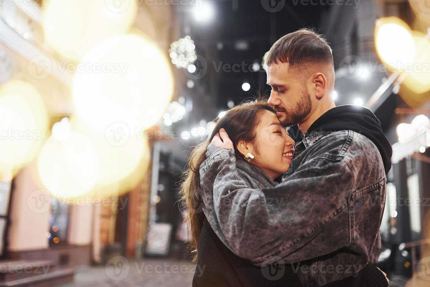 Abbracciare una persona ogni Altro. contento multirazziale coppia insieme all'aperto nel il città festeggiare nuovo anno foto