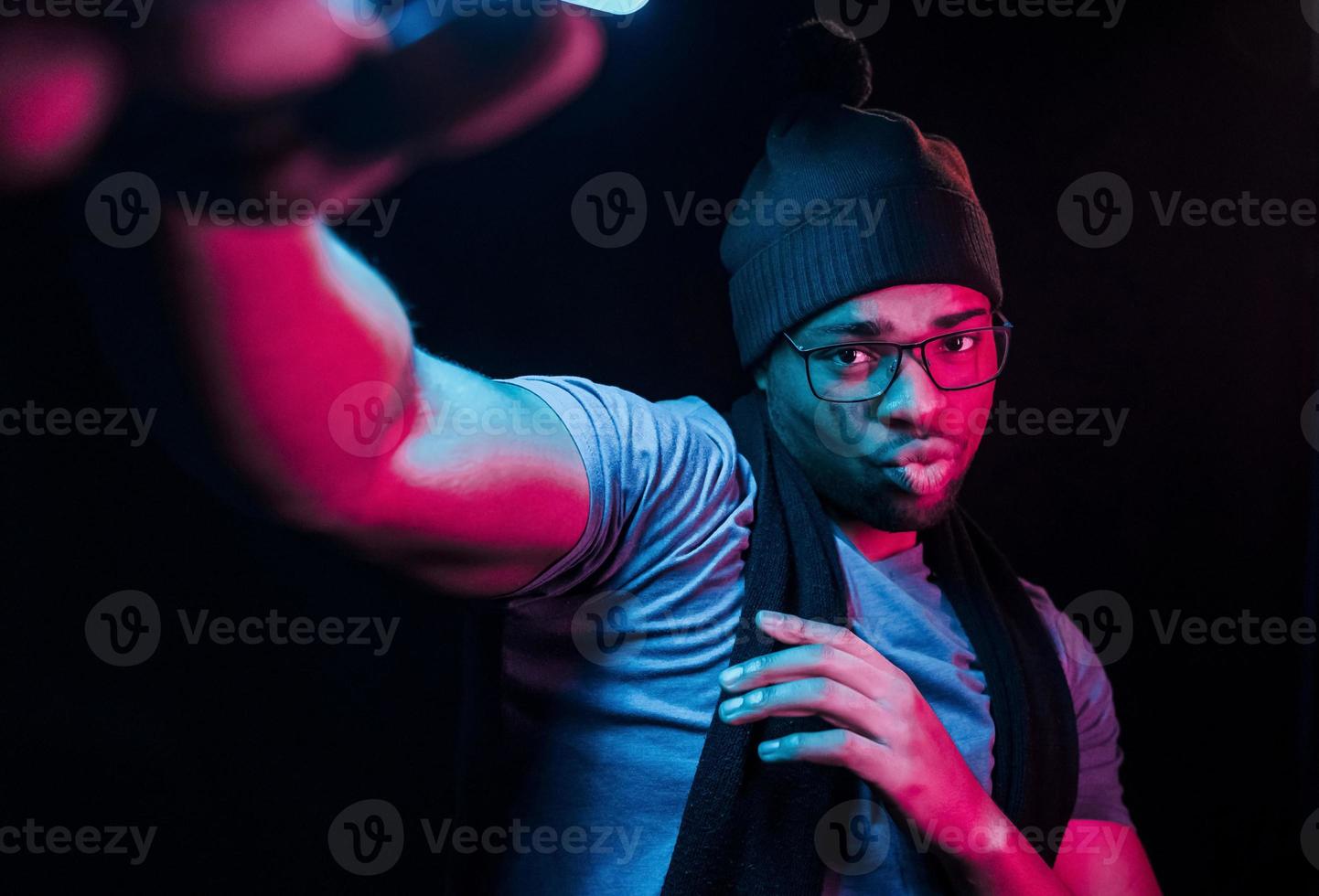 nel cappello e sciarpa. futuristico neon illuminazione. giovane africano americano uomo nel il studio foto