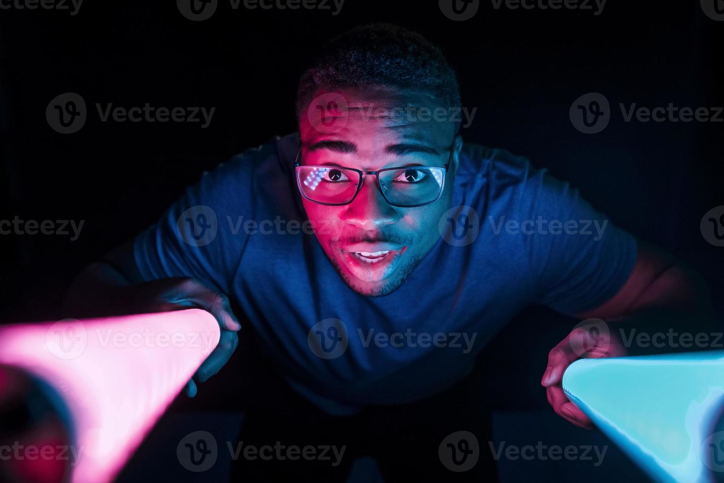 detiene illuminazione attrezzatura. futuristico neon illuminazione. giovane africano americano uomo nel il studio foto