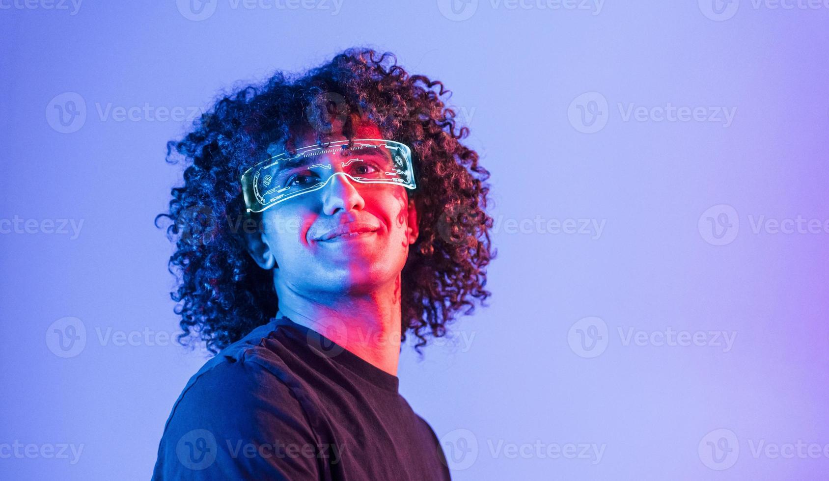 nel futuristico occhiali. giovane bellissimo uomo con Riccio capelli è in casa nel il studio con neon illuminazione foto