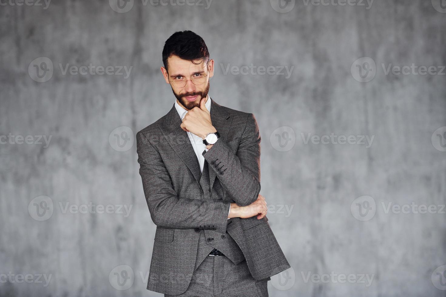 in piedi contro grigio sfondo. giovane elegante uomo d'affari nel completo da uomo al chiuso. concezione di successo foto