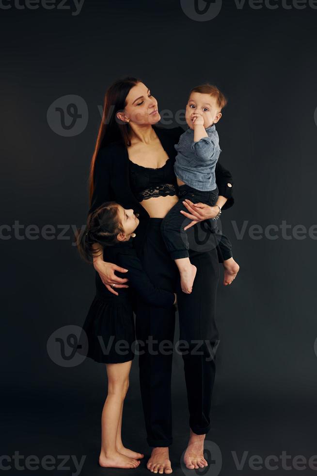 donna nel nero elegante Abiti è con sua poco figlio e figlia nel il studio foto