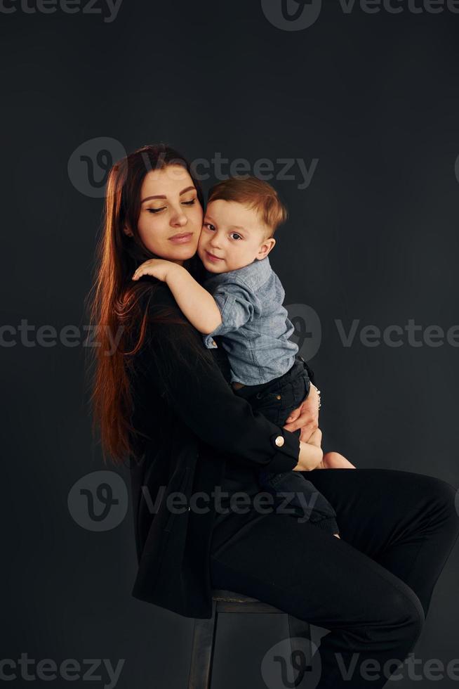 madre nel elegante nero Abiti è con sua poco figlio nel il studio foto