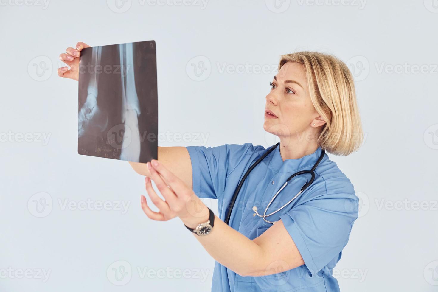 detiene raggi X. di mezza età professionale femmina medico nel uniforme e con stetoscopio foto