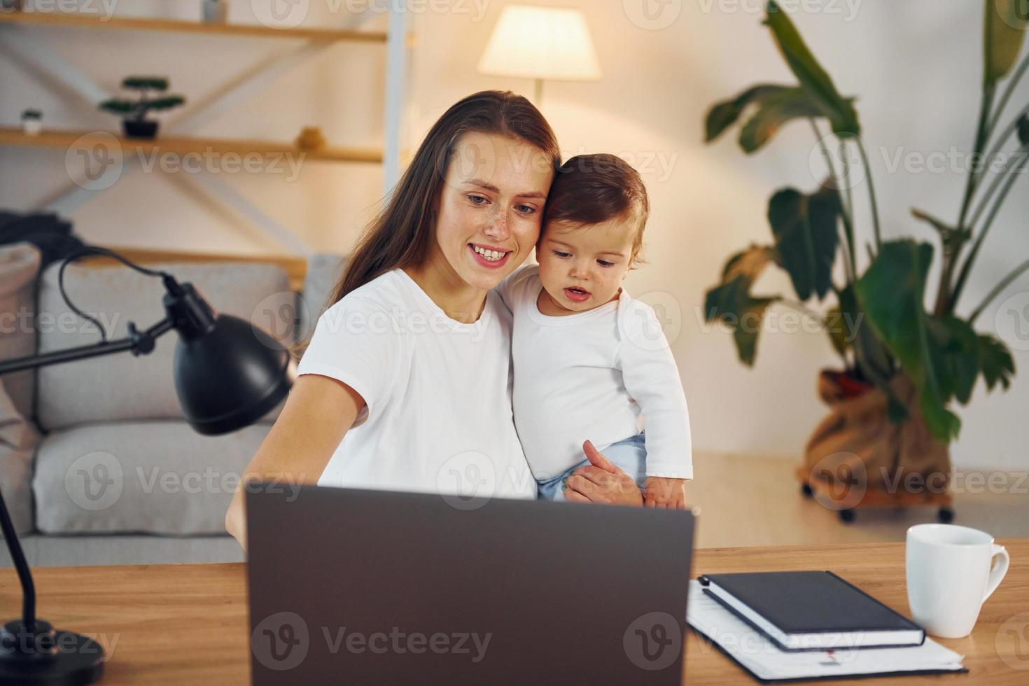 seduta di il tavolo con il computer portatile. madre con sua poco figlia è a casa insieme foto