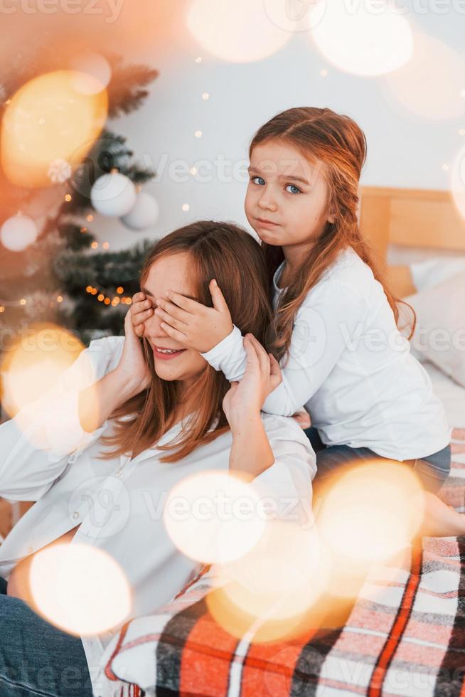 avendo divertimento. madre con sua poco figlia è avendo divertimento in casa su il letto foto